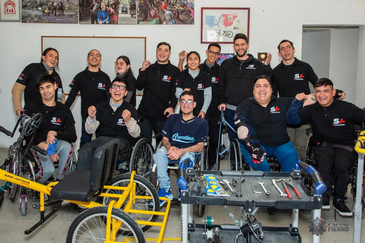 Gran grupo de integrantes del equipo sonriendo y posando juntos en el taller junto a bicicletas adaptadas y herramientas