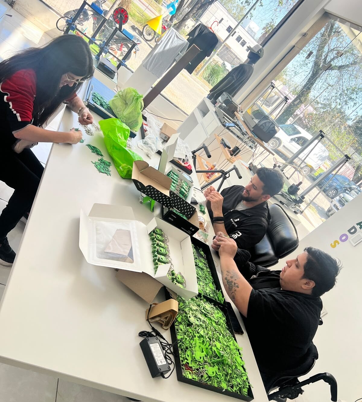 Tres personas trabajando en una mesa larga armando y preparando llaveros impresos en 3D en el taller"